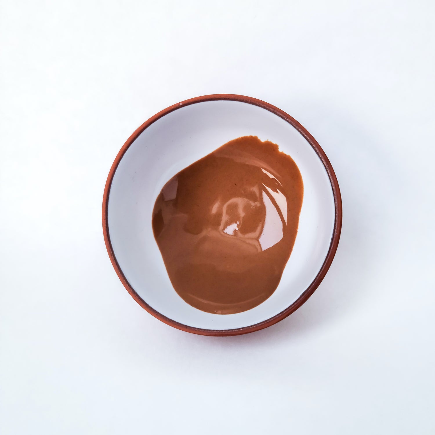 A small ceramic bowl filled with Erleia's Signature Clay Mask, a smooth, rich, brown paste used for deep cleansing and exfoliation.