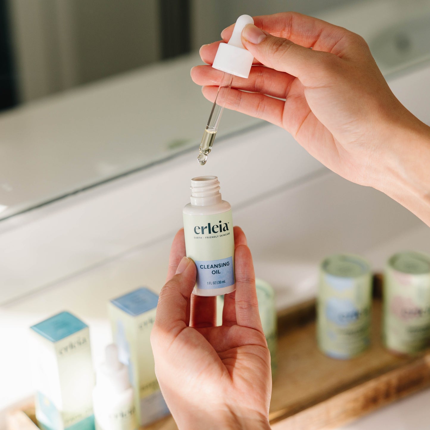 Erleia Cleansing Oil with the dropper open and product being used by two light skinned hands