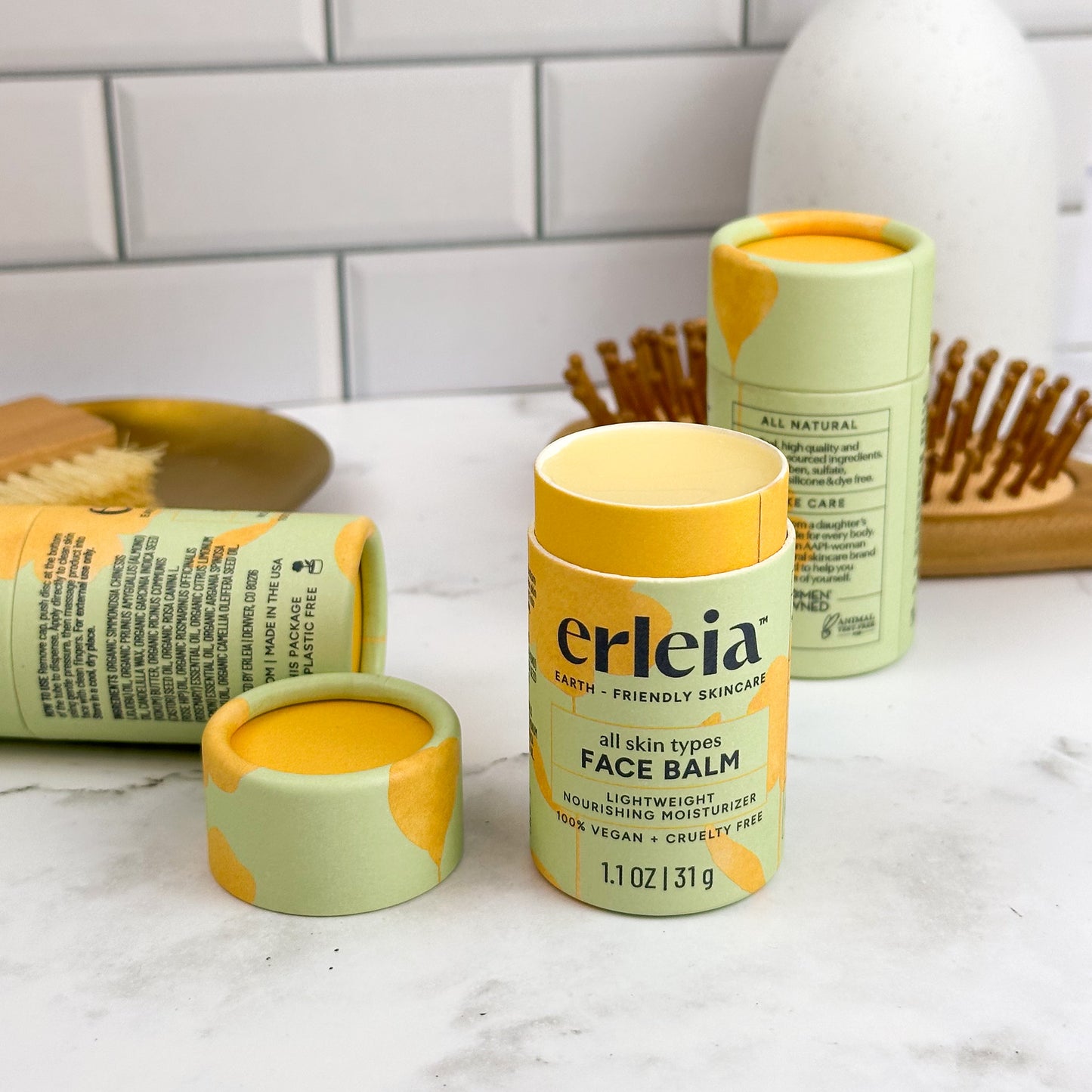 Erleia all skin types Face Balms on a bathroom counter, one is open and uncapped showing a light beige shiny balm