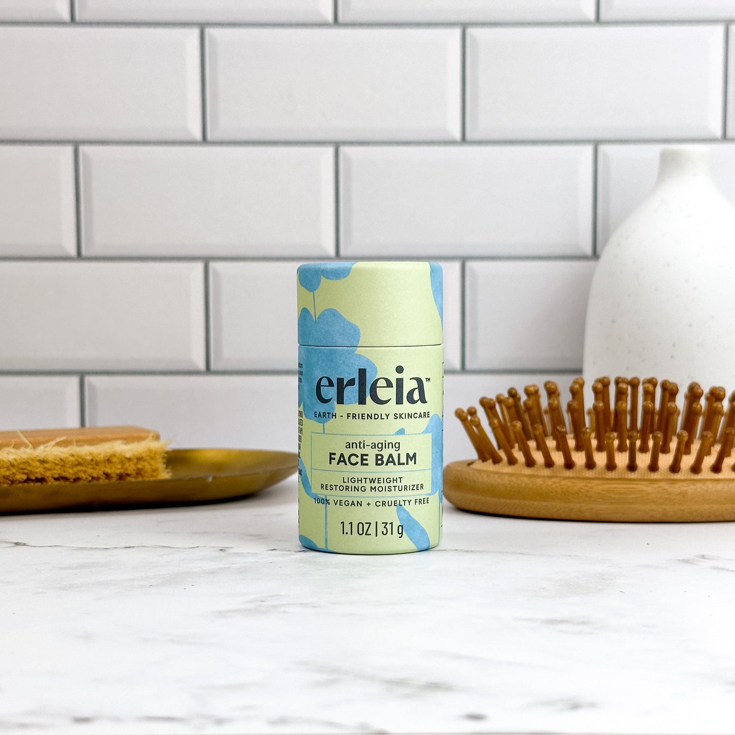 Erleia Anti-Aging Face Balm is placed on a white countertop, with a wooden brush and dish in the background. The packaging highlights its vegan, cruelty-free formula designed for deep cleaning and exfoliation.