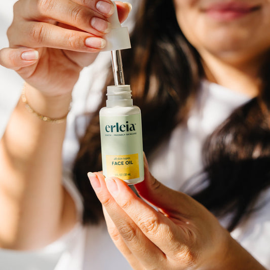 An Erleia All Skin Types Face Oil is in focus, as a light skinned Latina woman opens the dropper