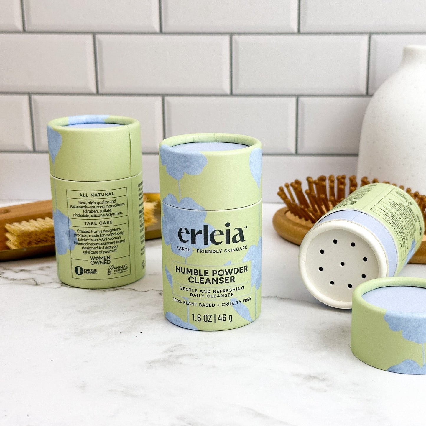 Multiple containers of Erleia Humble Powder Cleanser on a bathroom counter - one is open, showing the shaker dispenser top