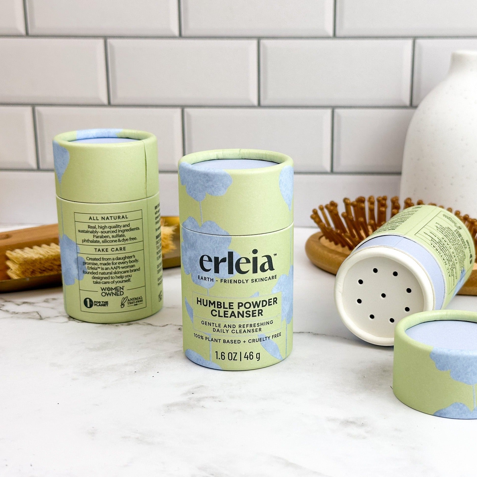 Multiple containers of Erleia Humble Powder Cleanser on a bathroom counter - one is open, showing the shaker dispenser top
