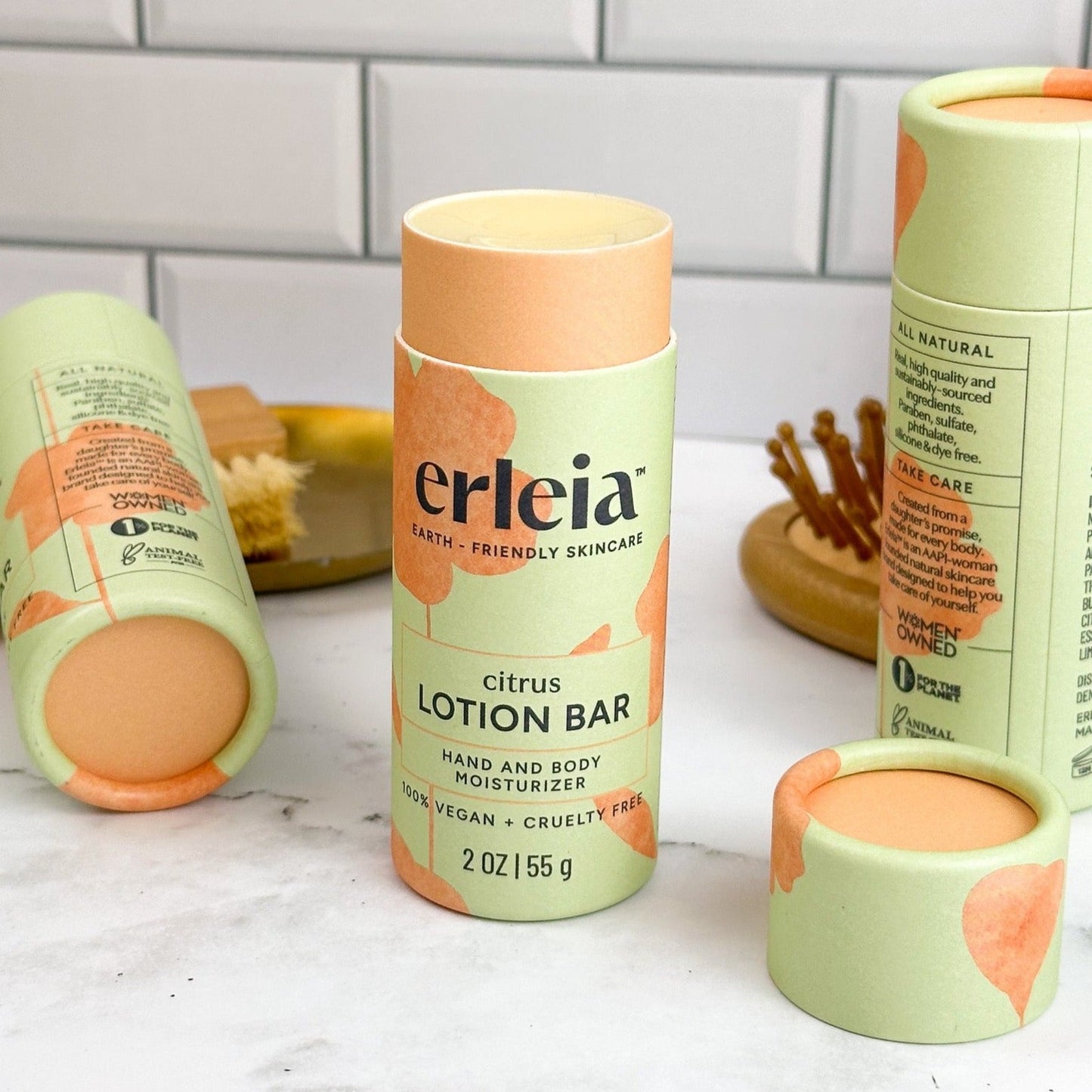 An Erleia citrus lotion bar, open and uncapped on a white marble bathroom counter with accessories in the background