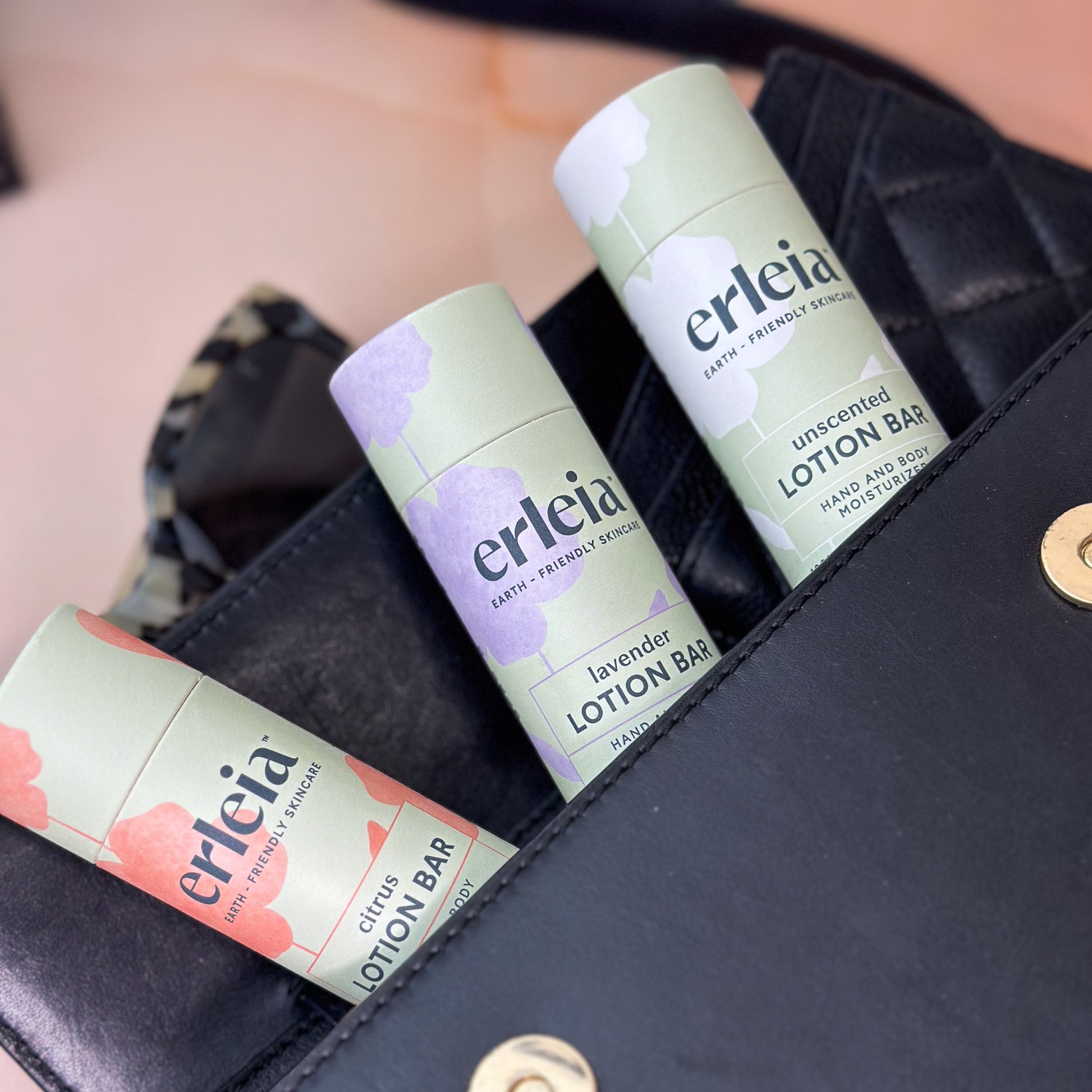 3 Erleia lotion bars in citrus, lavender and unscented scents, in a black purse - with accessories peeking out of the purse