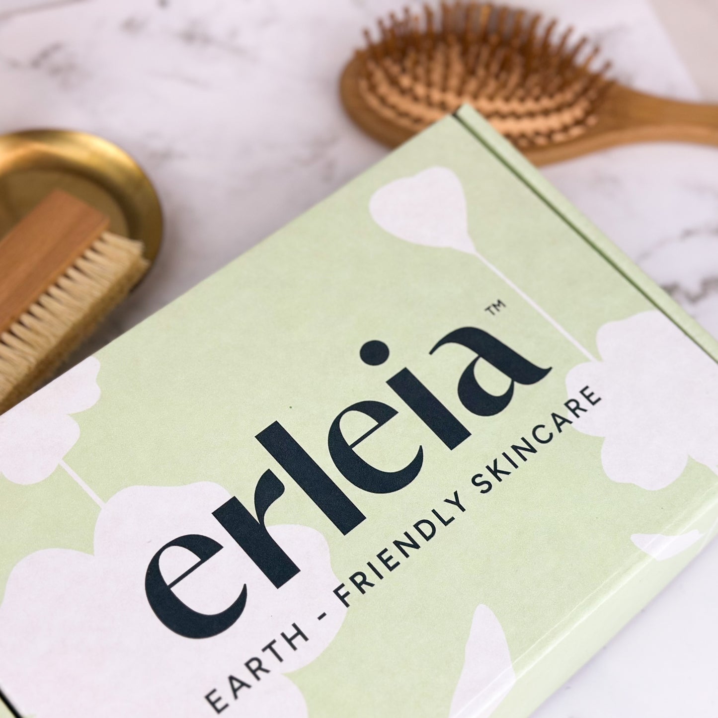 An Erleia Earth-Friendly Skincare box is featured with a wooden foot brush and hairbrush in the background, showcasing an eco-conscious skincare and self-care theme.