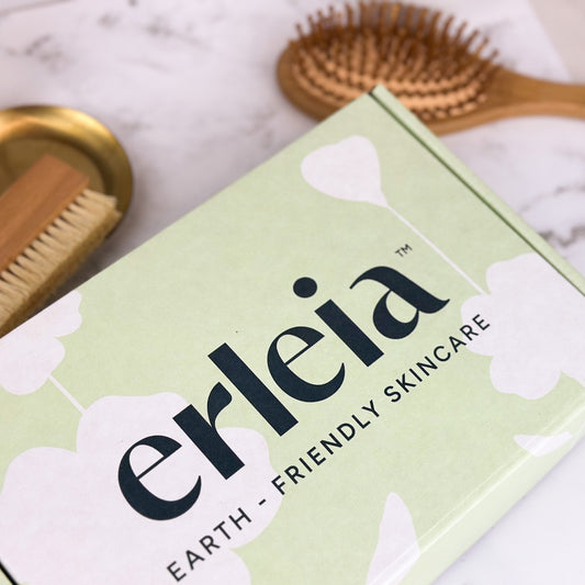 An Erleia Earth-Friendly Skincare box is featured with a wooden foot brush and hairbrush in the background, showcasing an eco-conscious skincare and self-care theme.