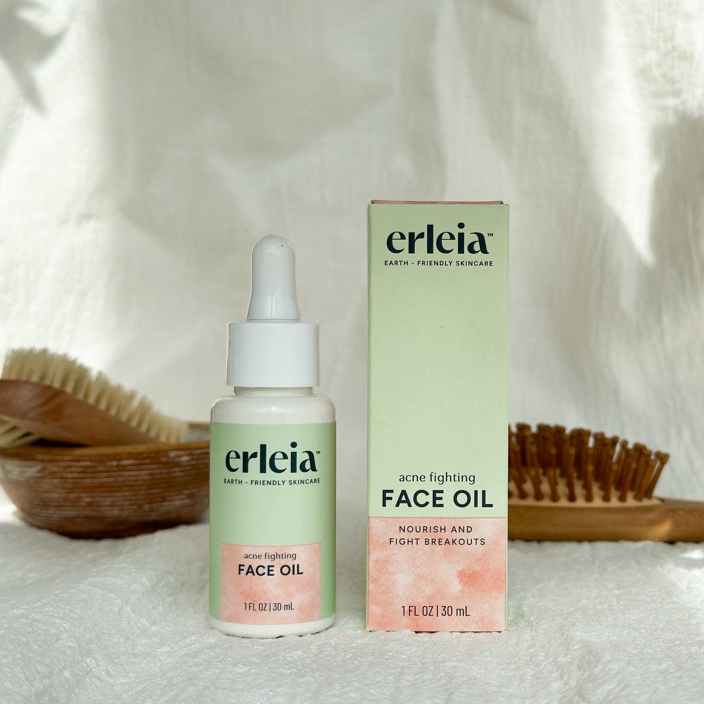 Erleia Face Oil - Acne Fighting Bottle and Box on a white warm background with shadows and bathroom items in the background