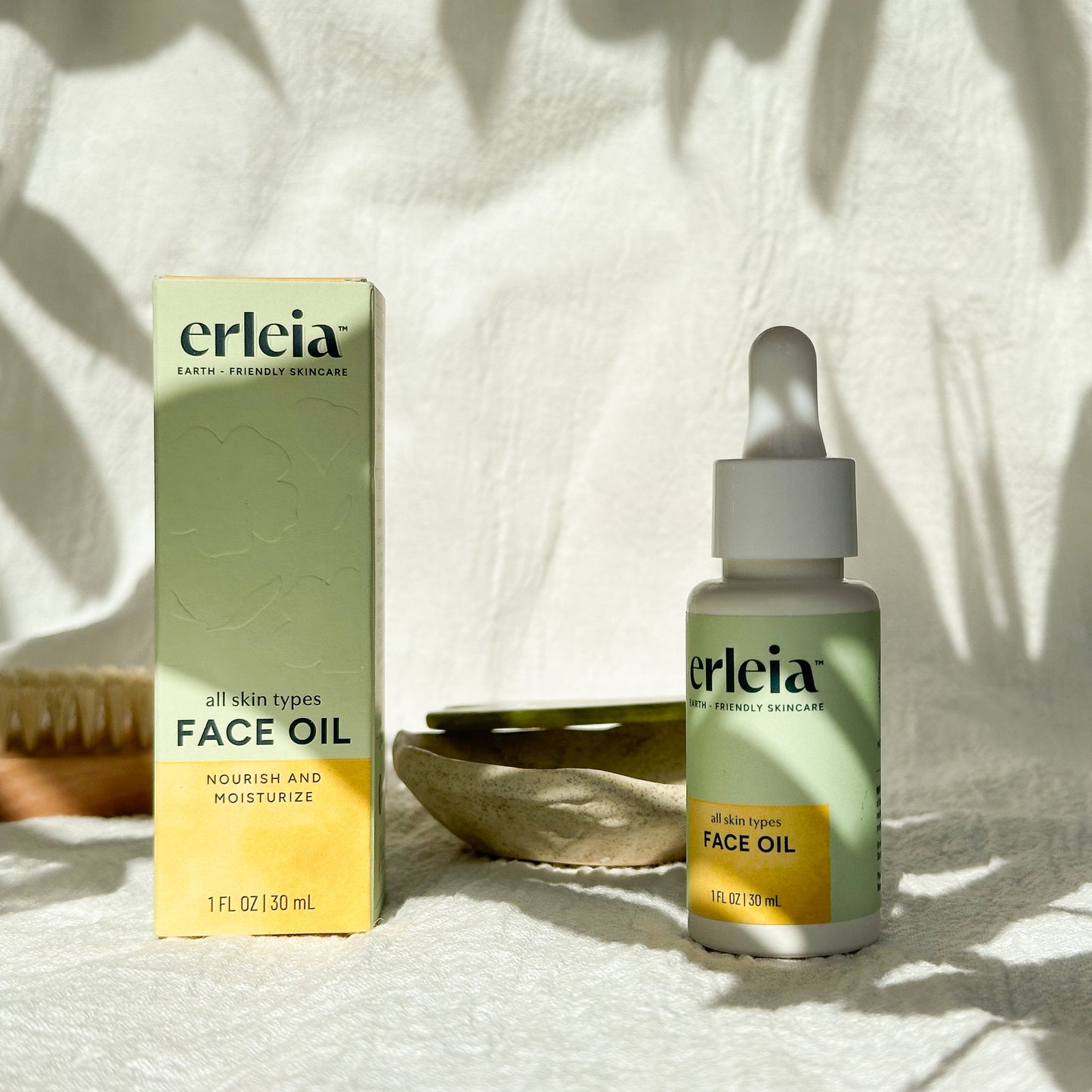 Erleia Face Oil - All Skin Types Bottle and Box on a white warm background with shadows and bathroom items in the background