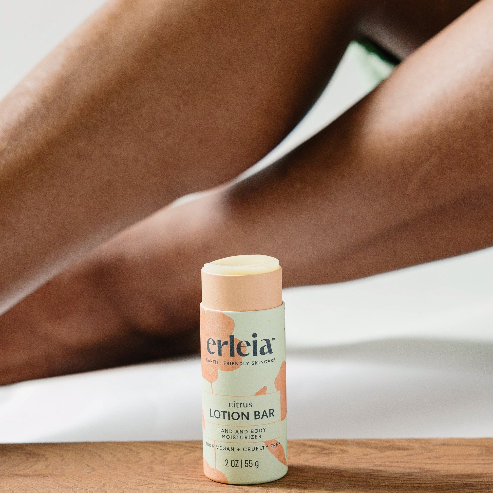 An Erleia citrus lotion bar, uncapped and open, being used on a Black woman's legs