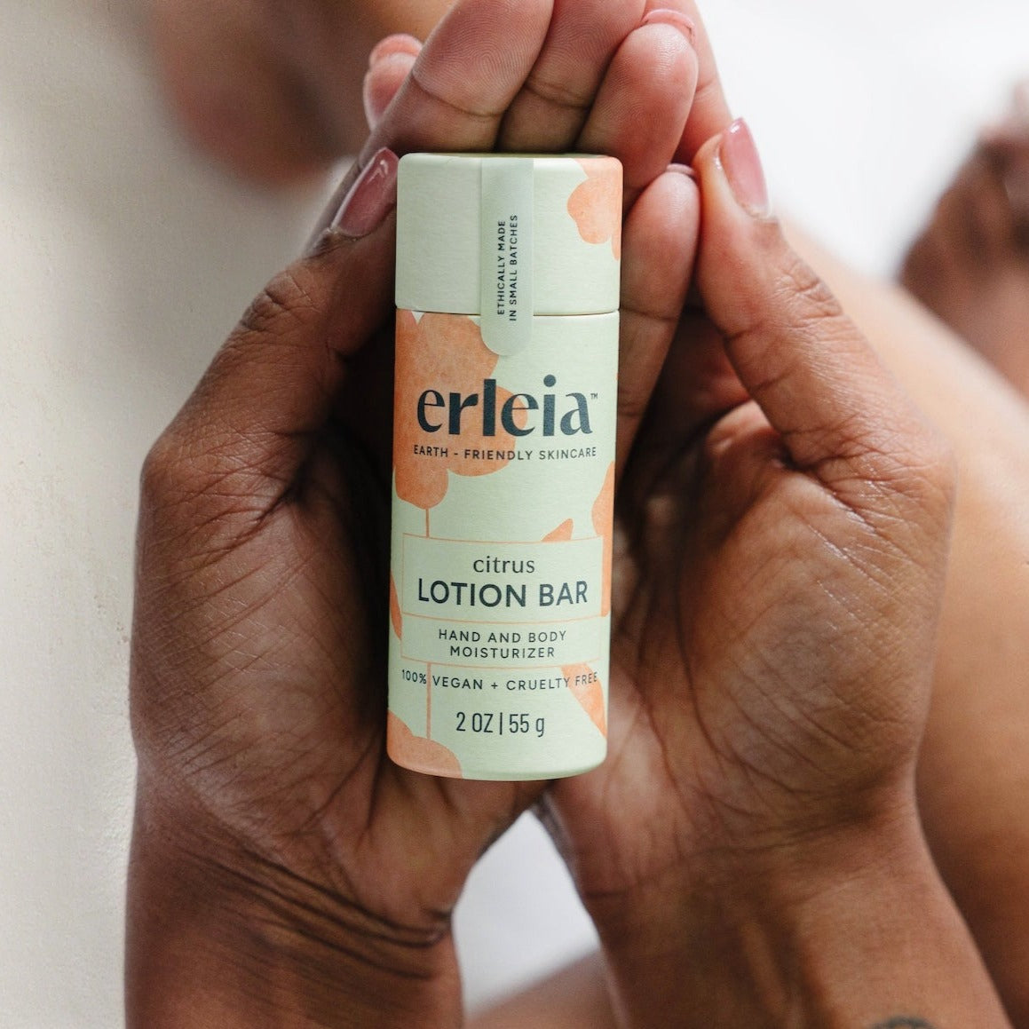 An Erleia citrus lotion bar held by two Black hands