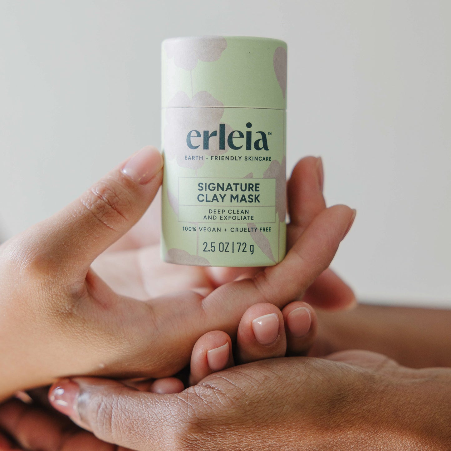 East Asian and Black hands holding an Erleia Signature Clay Mask