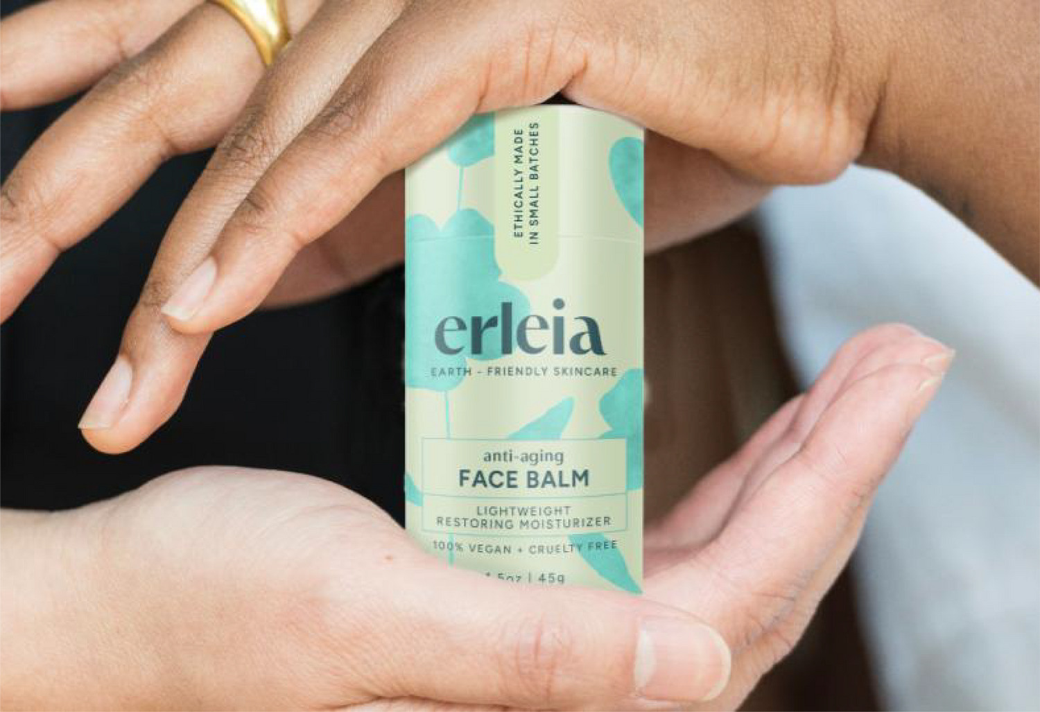 Hands gently hold a container of Erleia's anti-aging face balm, a lightweight restoring moisturizer that is 100% vegan and cruelty-free.