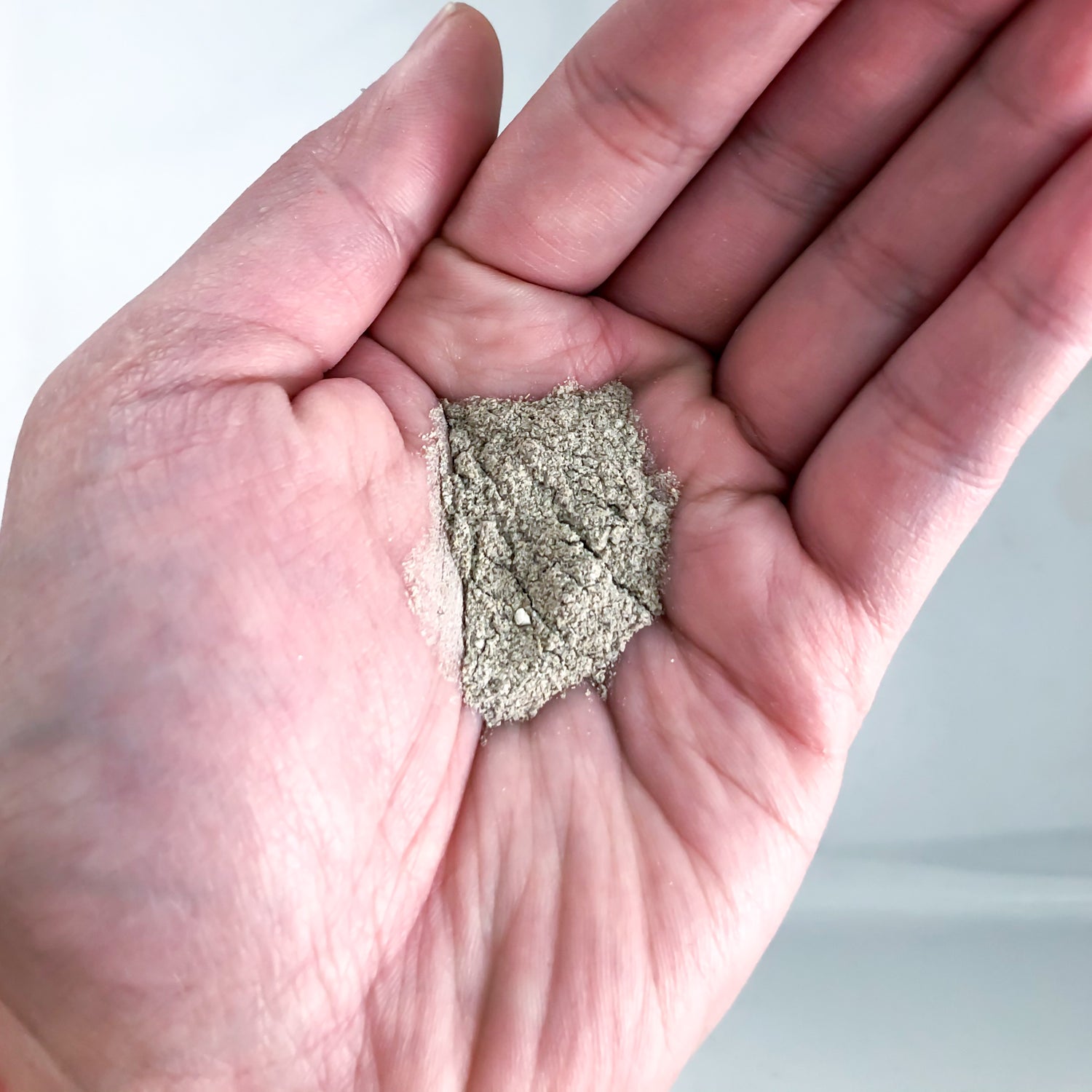 A hand holding a small amount of Erleia Humble Cleansing Powder, ready to be used as part of a skincare or beauty routine.