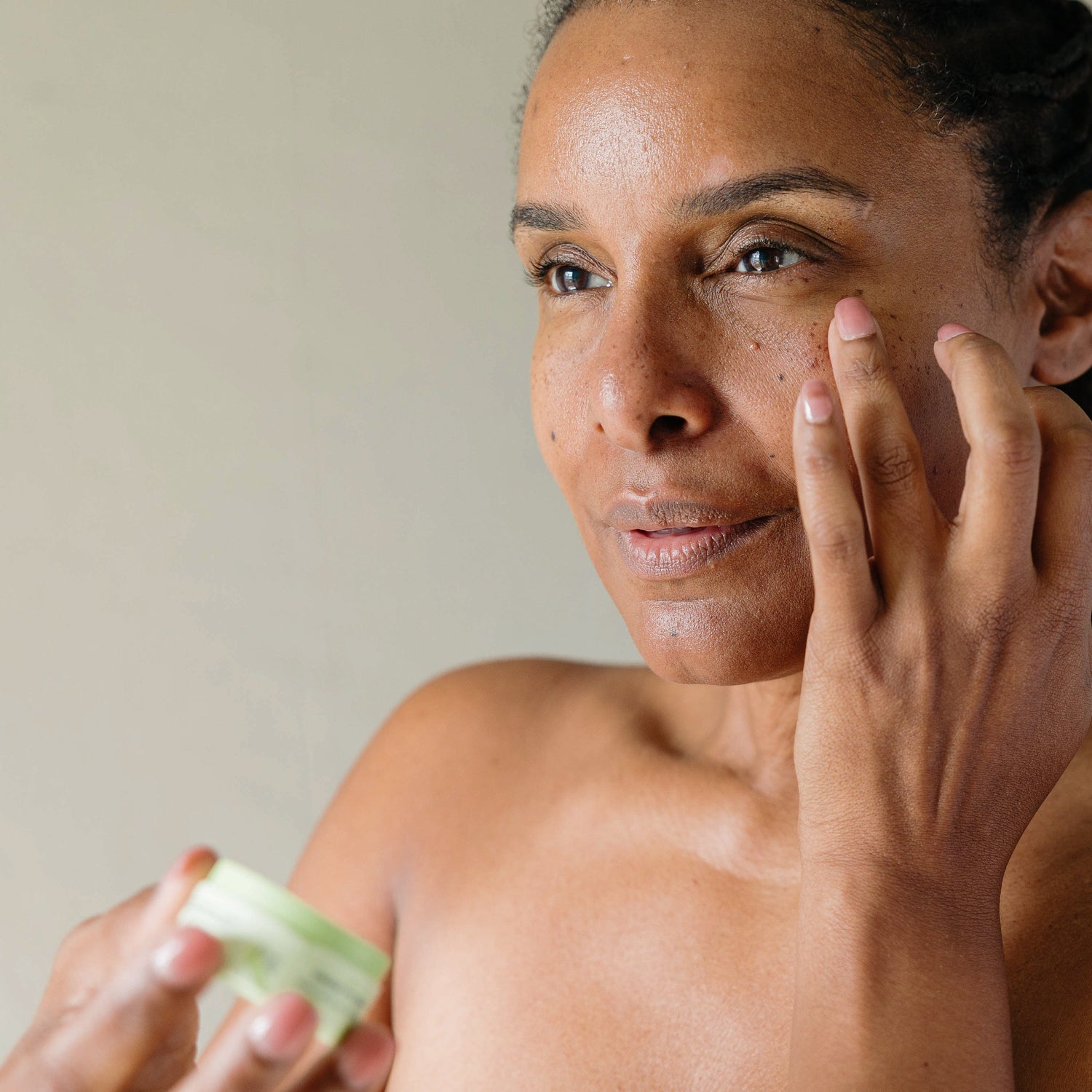 A Black woman using Erleia Under Eye Balm - using her ring finger, she gently applies product to her face