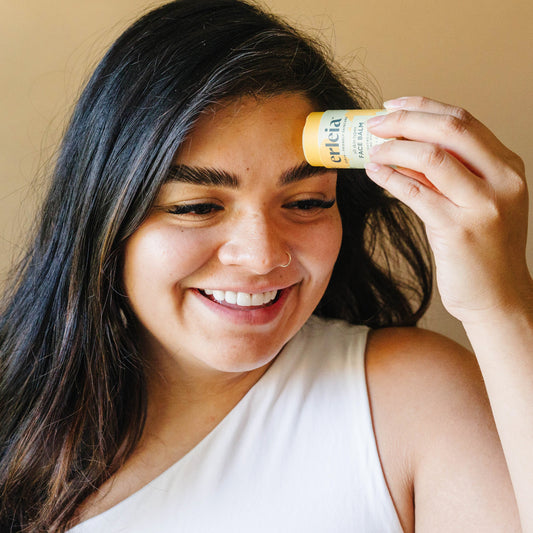 A light skinned Latina woman applying Erleia All Skin Types Face Balm to her forehead