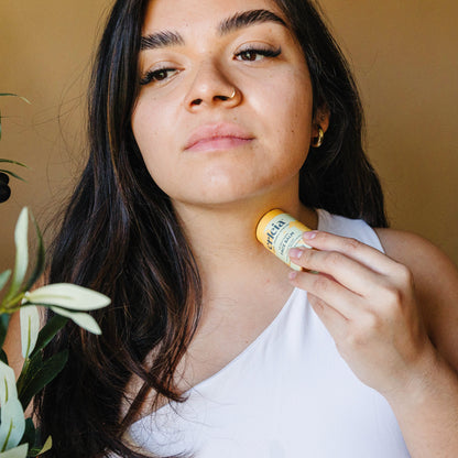 A light skinned Latina woman applying Erleia All Skin Types Face Balm to her neck