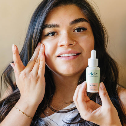 A light skinned Latina woman applying Erleia Acne Fighting Face Oil to her cheek