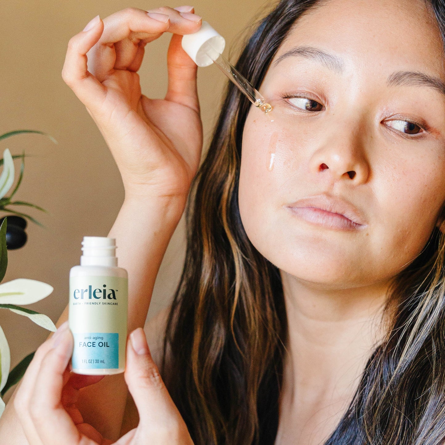 An East Asian woman applying Erleia Anti-Aging Face Oil to her cheek with a dropper