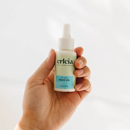 A light skinned hand holding an Erleia Anti-Aging Face Oil bottle in a white background