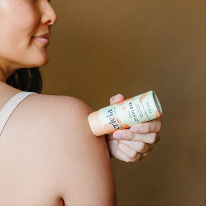 An East Asian woman applying an Erleia Citrus Lotion Bar to her shoulder