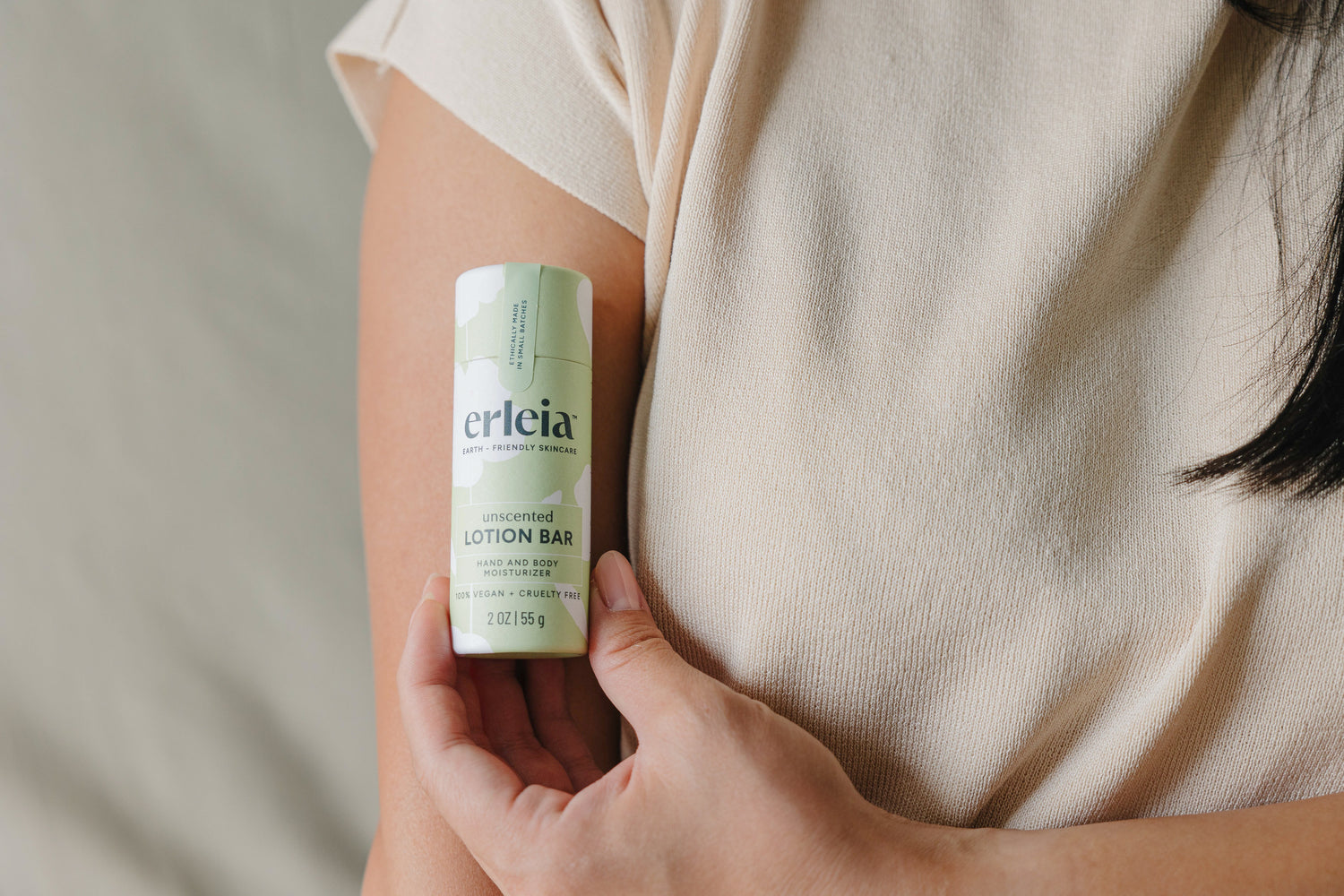 A person holds an Erleia unscented lotion bar against their arm, wearing a soft beige shirt.