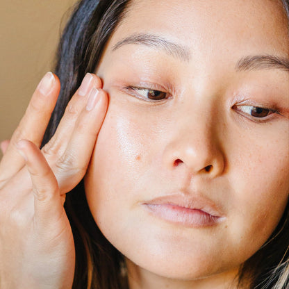 An East Asian woman applying product to her cheekbone with her fingers