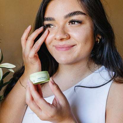 A light skinned Latina woman applying Erleia Under Eye Balm to her under eye area with her ring finger