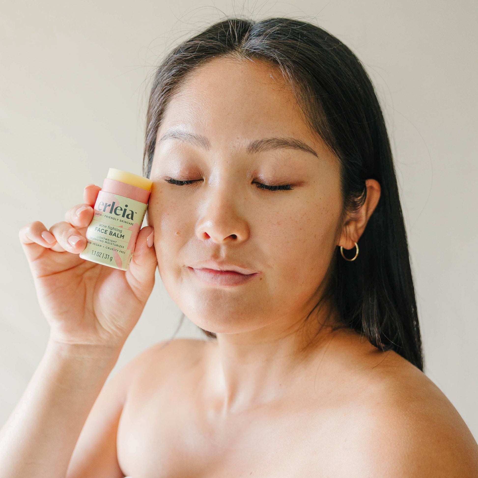 An East Asian woman holding an Erleia acne fighting Face Balm to her cheek