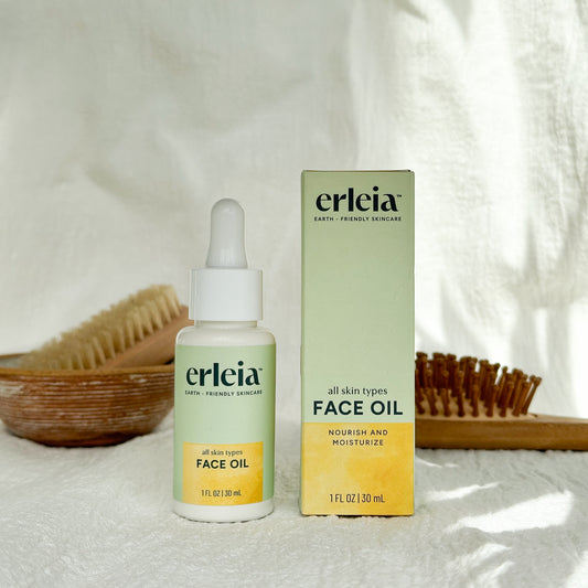 Erleia Face Oil - All Skin Types Bottle and Box on a white warm background with shadows and bathroom items in the background