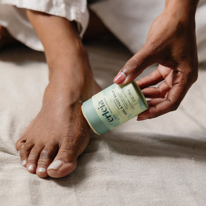 A Black woman applying Erleia eucalyptus Heel & Foot Balm to her foot