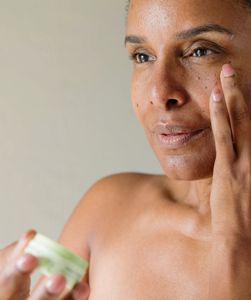 A Black woman applying Erleia Under Eye Balm to her undereye area