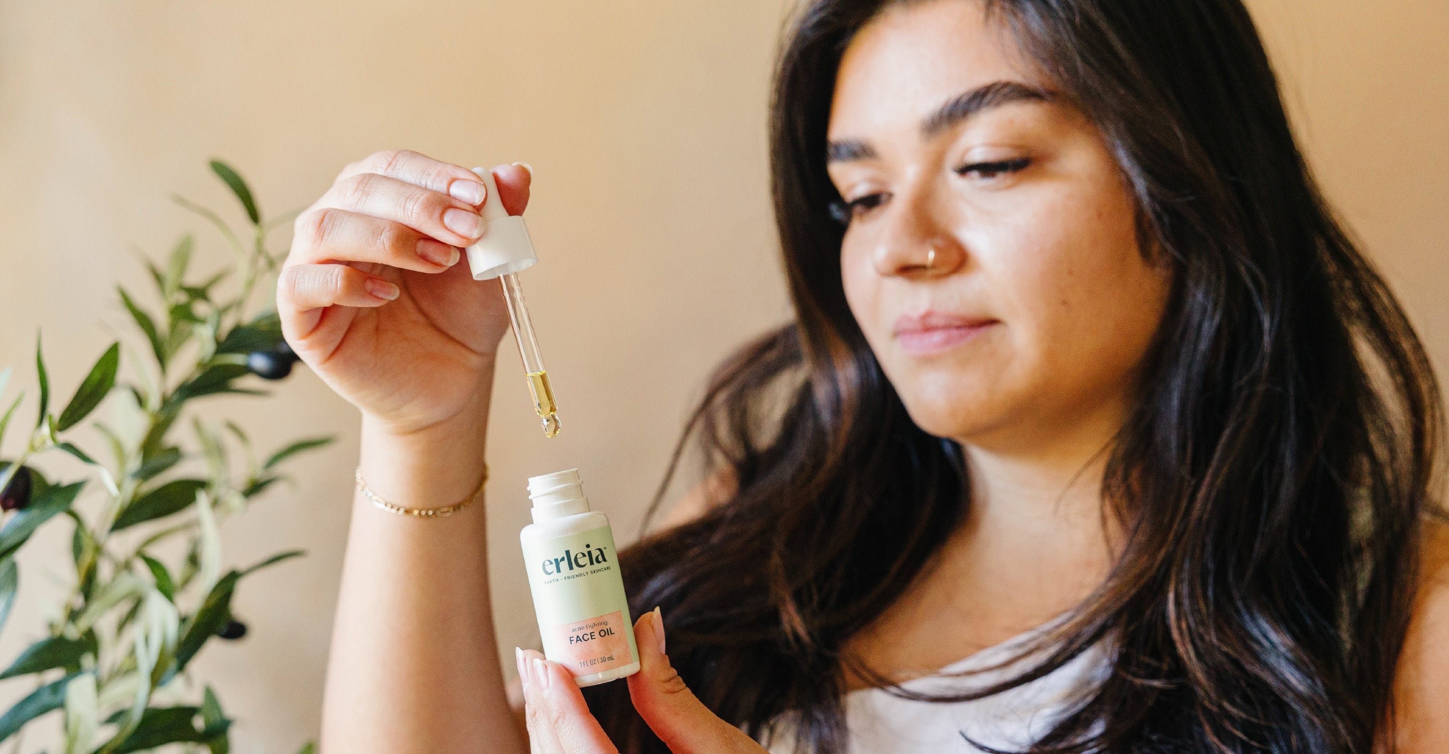 A Latina woman holding an Erleia Face Oil bottle and dropper
