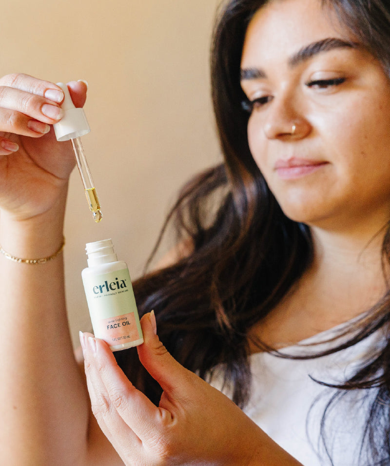 A Latina woman holding an Erleia Face Oil bottle and dropper