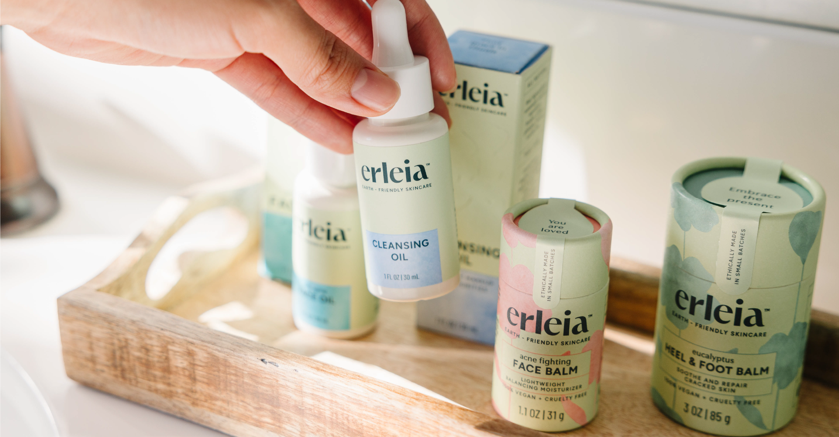 An Erleia Cleansing Oil being picked up by a hand from a tray with other Erleia products