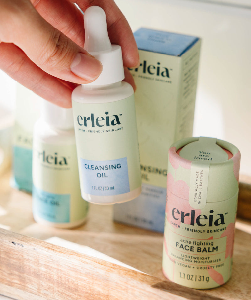 An Erleia Cleansing Oil being picked up by a hand from a tray with other Erleia products