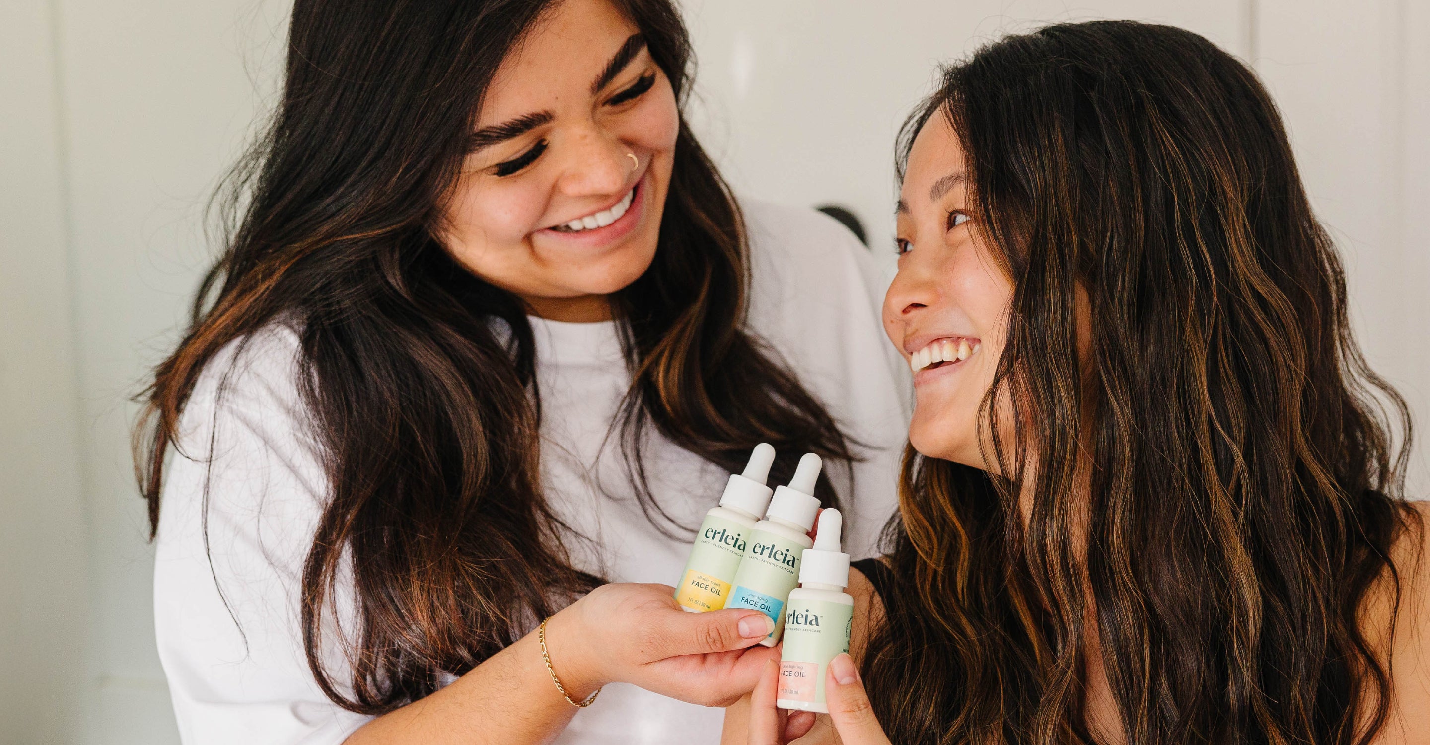 Two women holding Erleia skincare bottles and smiling