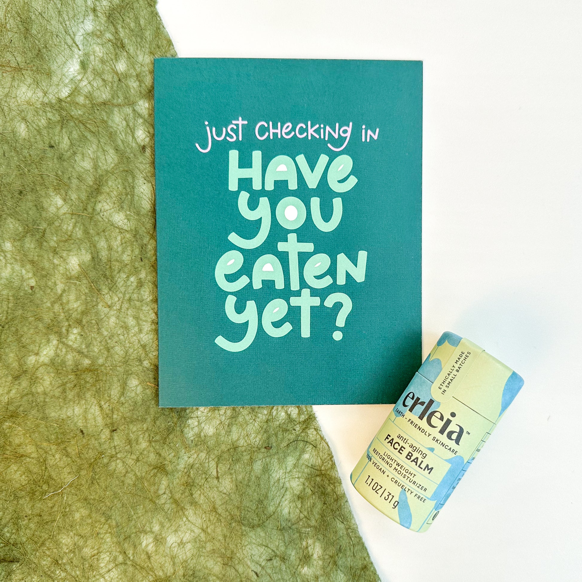 Erleia’s acne-fighting face balm is displayed next to a card that reads "Just checking in. Have you eaten yet?" promoting care and concern for a loved one’s well-being.