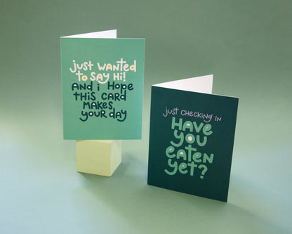 Two greeting cards, one says "just wanted to say hi! and I hope this card makes your day" the other says "just checking in, have you eaten yet?"