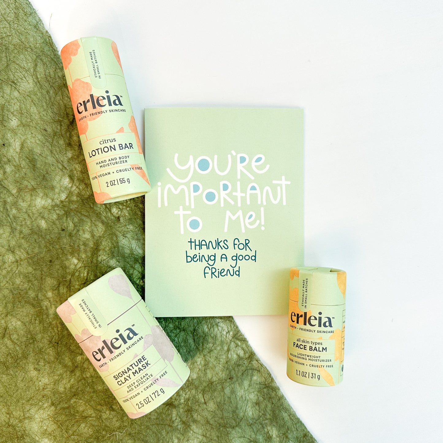 Erleia skincare products, including citrus lotion bar, signature clay mask, and face balm, are arranged around a card reading "You're important to me! Thanks for being a good friend," emphasizing self-care and friendship.