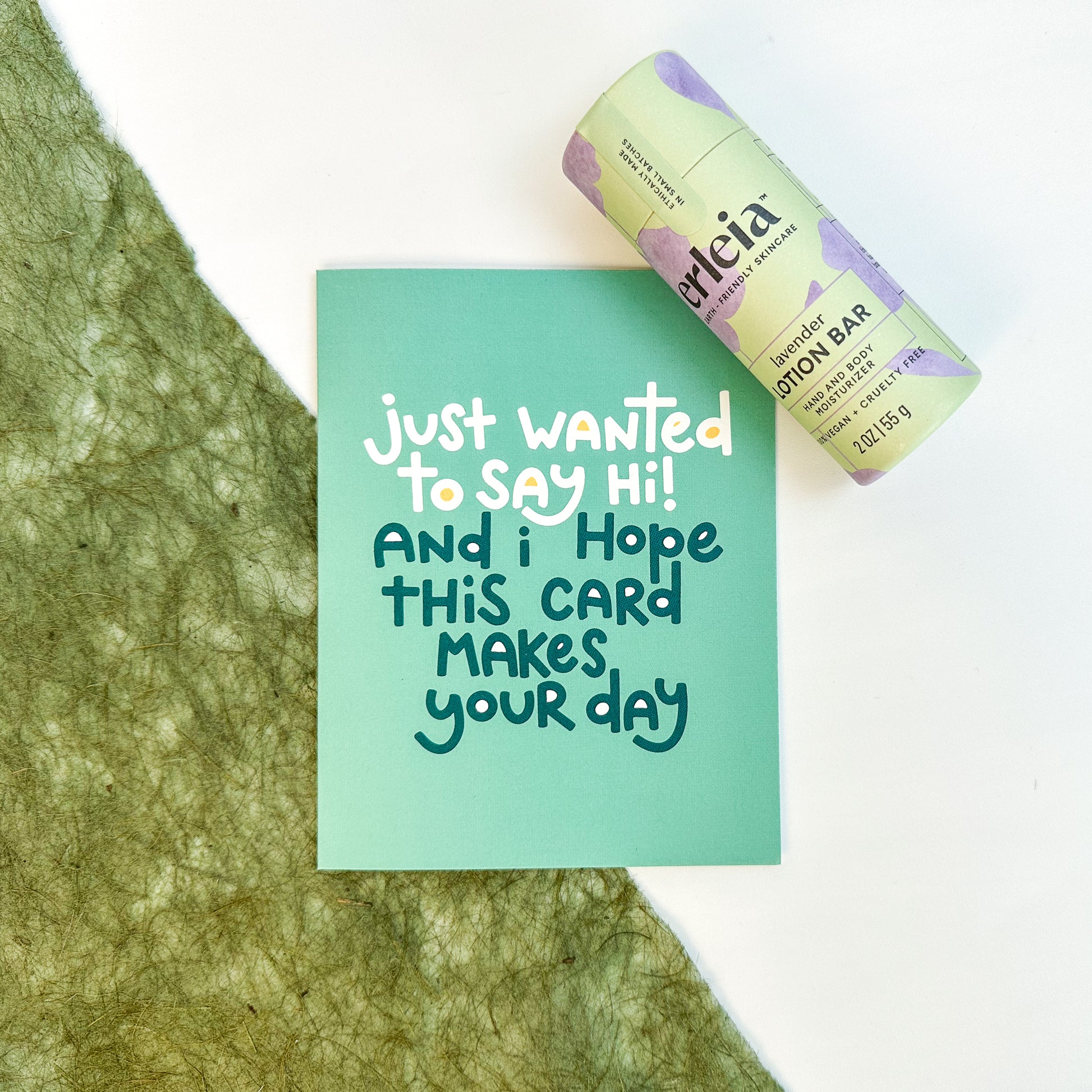 An Erleia lavender lotion bar is displayed next to a card that reads "Just wanted to say hi! And I hope this card makes your day," emphasizing a thoughtful gesture of care and connection.