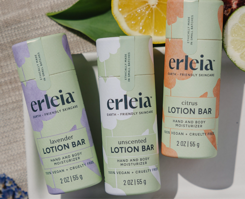 Erleia lotion bars in lavender, unscented, and citrus varieties are displayed on a white tray alongside slices of fresh citrus, emphasizing their 100% vegan and cruelty-free formulations.