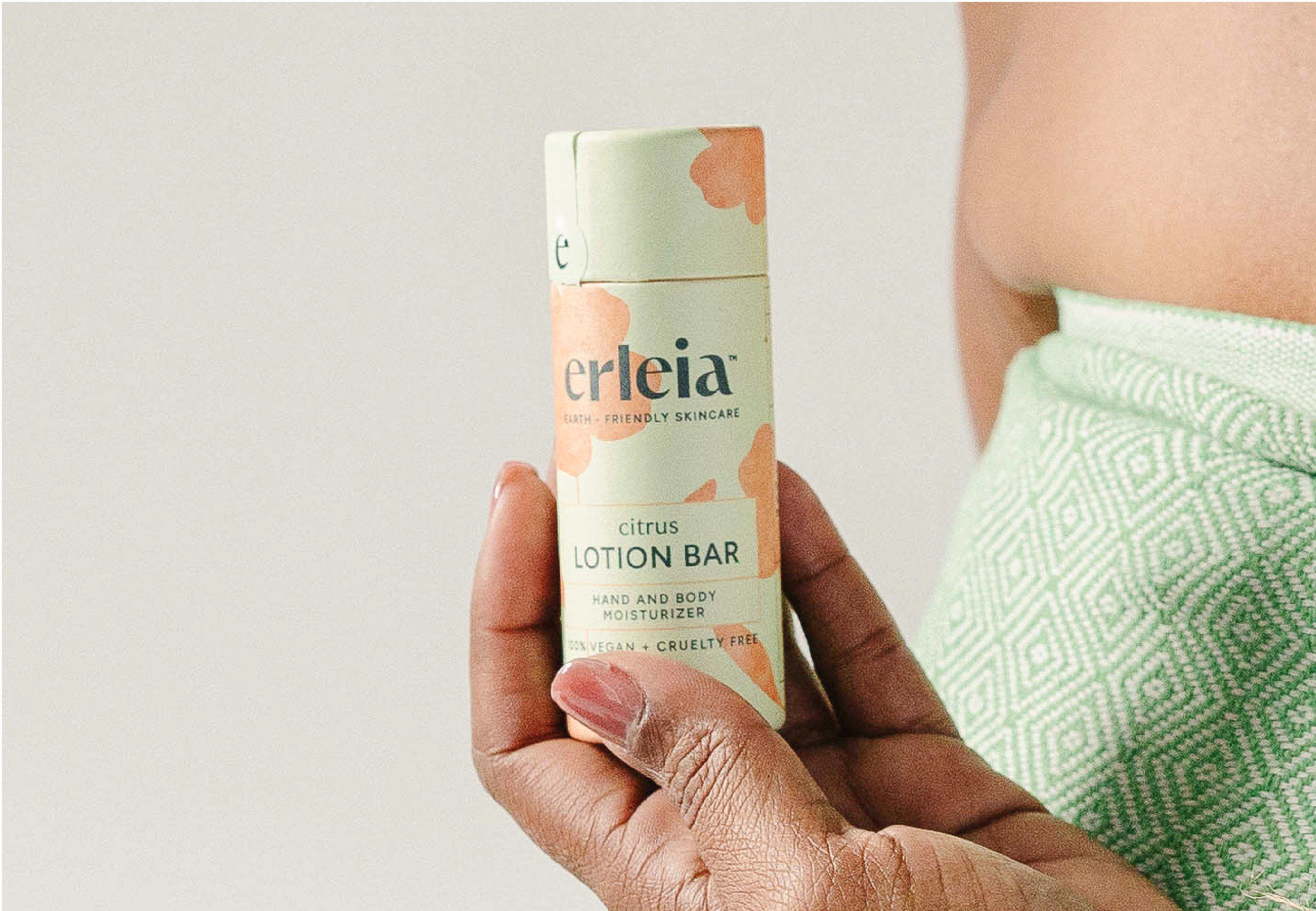 A person wrapped in a green towel holds an Erleia citrus lotion bar in eco-friendly packaging.