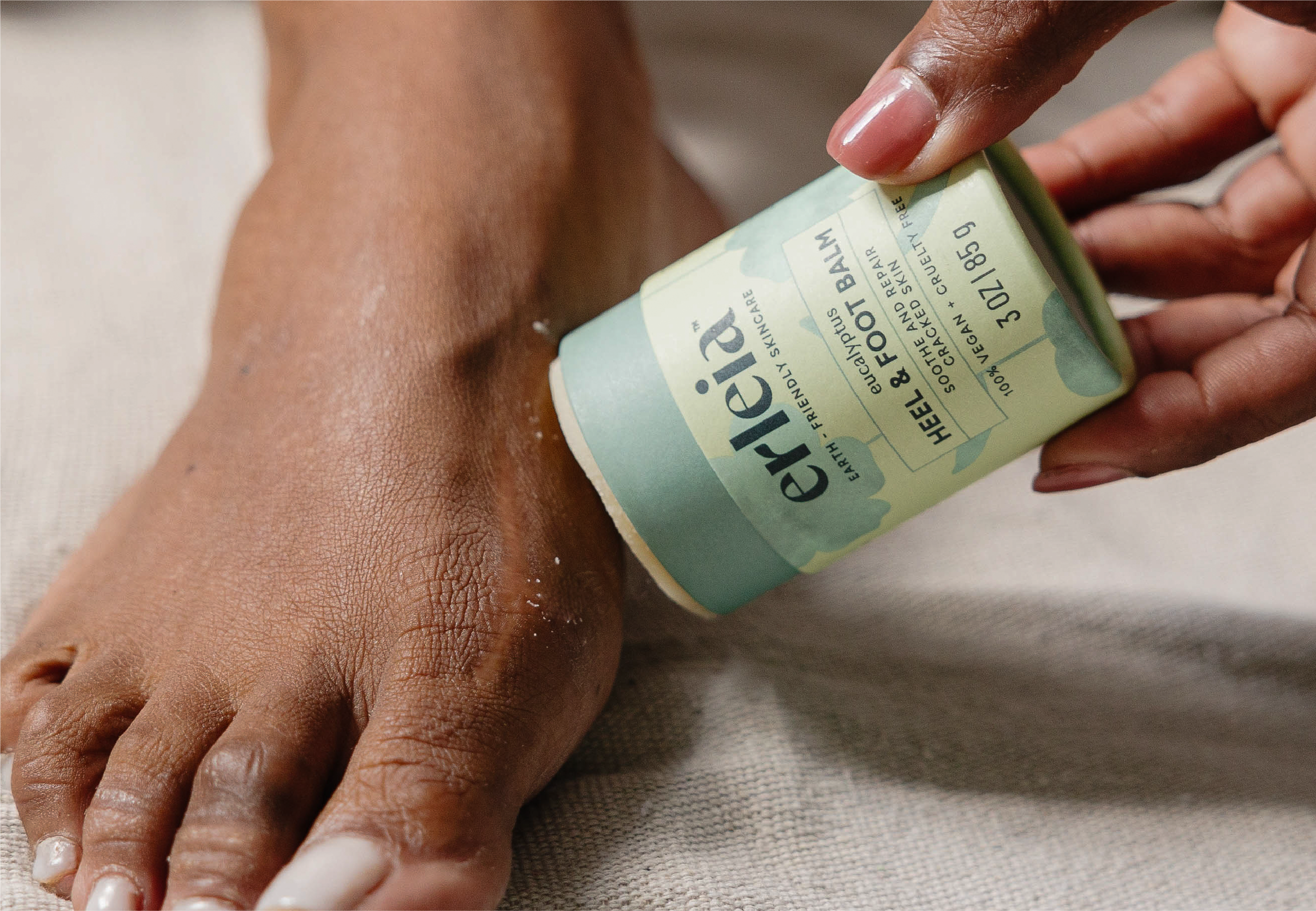 A person applies Erleia eucalyptus heel and foot balm to the top of their foot, showing the product's eco-friendly packaging.