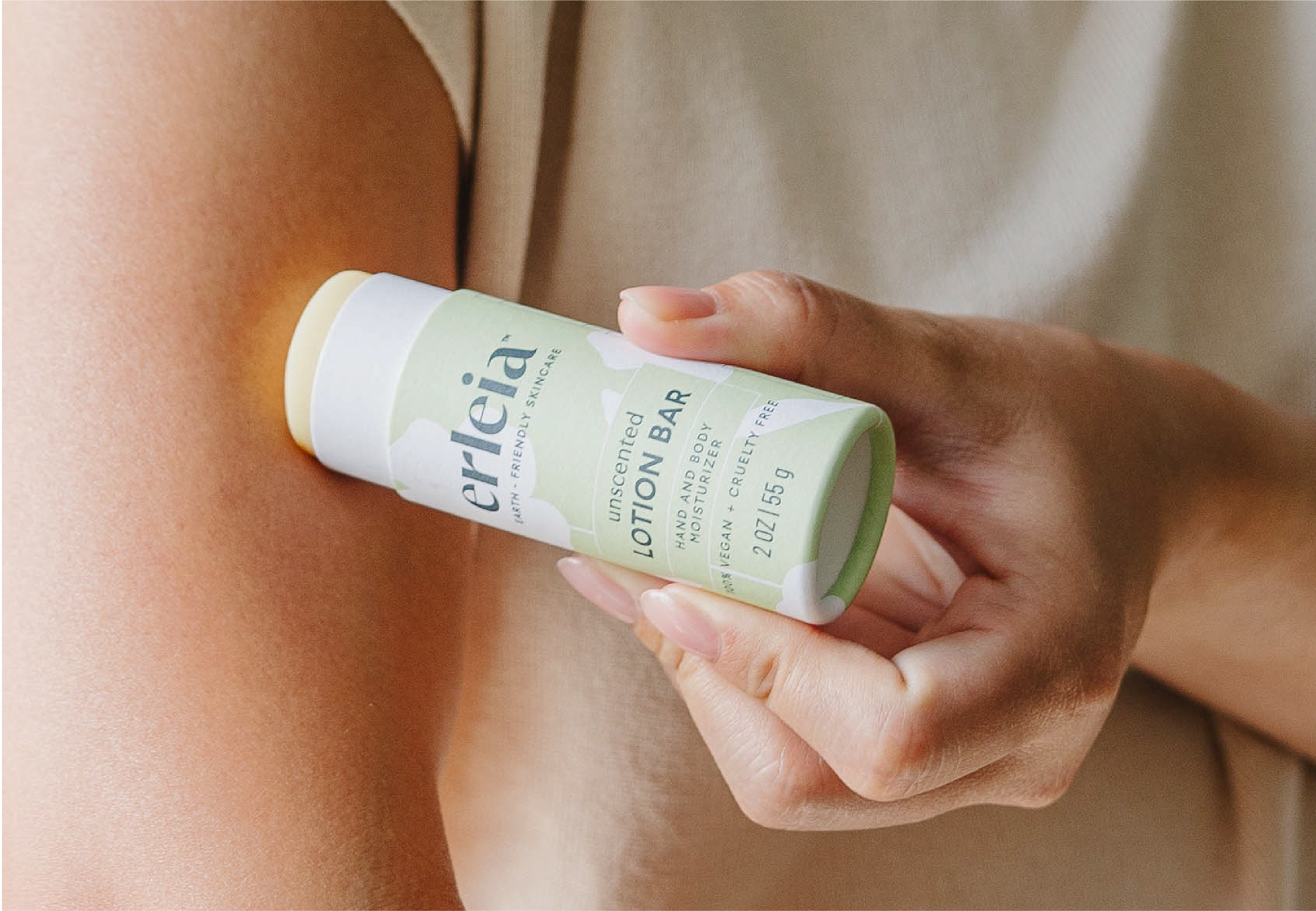 A person applies an Erleia unscented lotion bar to their arm, showing the product’s eco-friendly, minimalist green packaging.